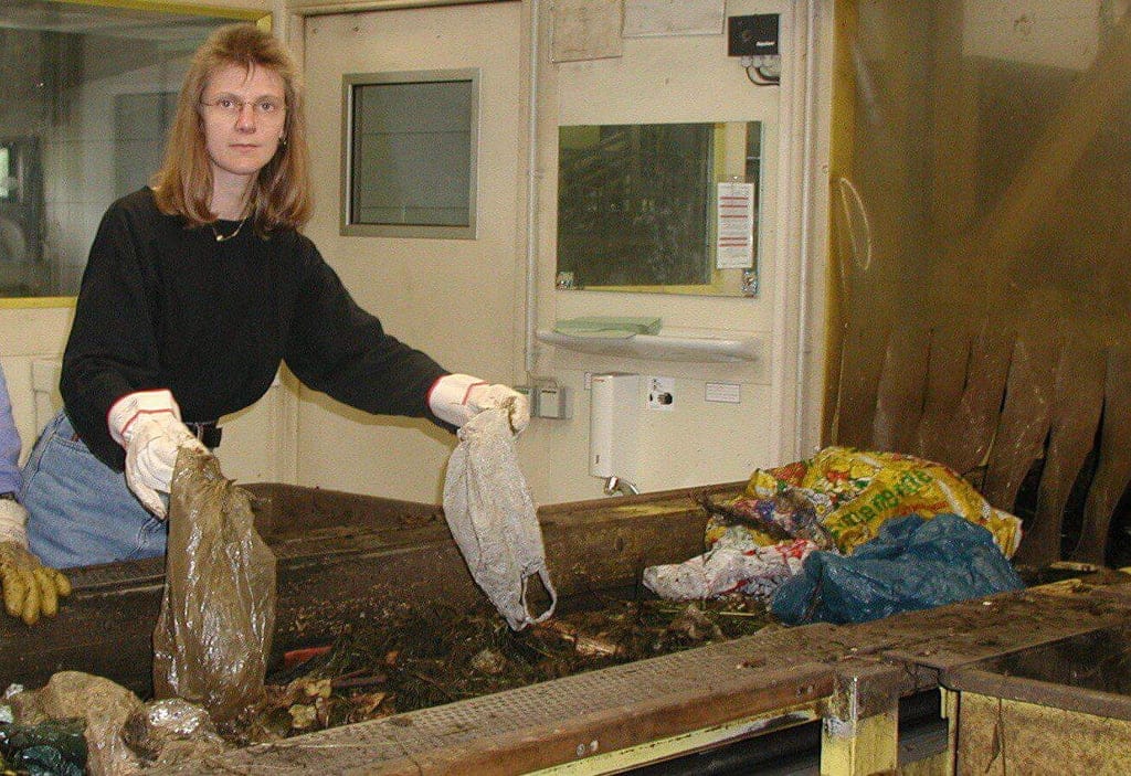 Frau hält falsch entsorgte Plastiktüten während der Handsortierung des Biomülls am Fließband in der Biokompostieranlage WGV Quarzbichl