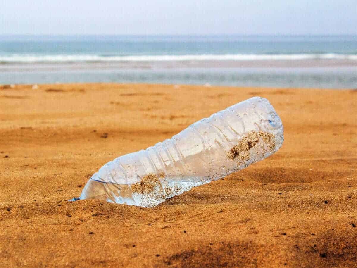 Plastik PET Flasche am Strand im Sand mit Meer im Hintergrund