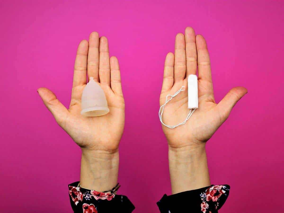 Menstruationstasse und Tampon auf Handfläche