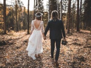 Boho Brautpaar von hinten Händchen haltend im Wald