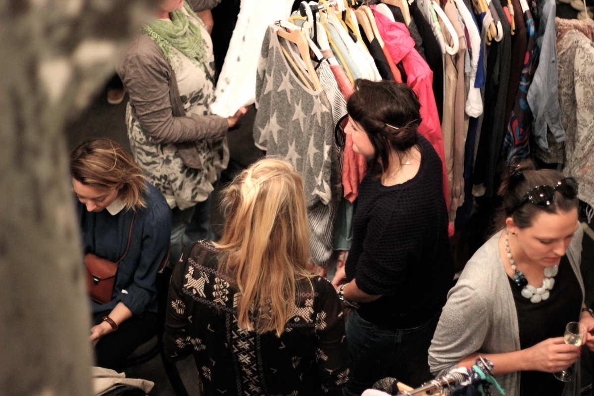Frauen auf einem Flohmarkt stehen neben viel Kleidung auf einem Kleiderständer