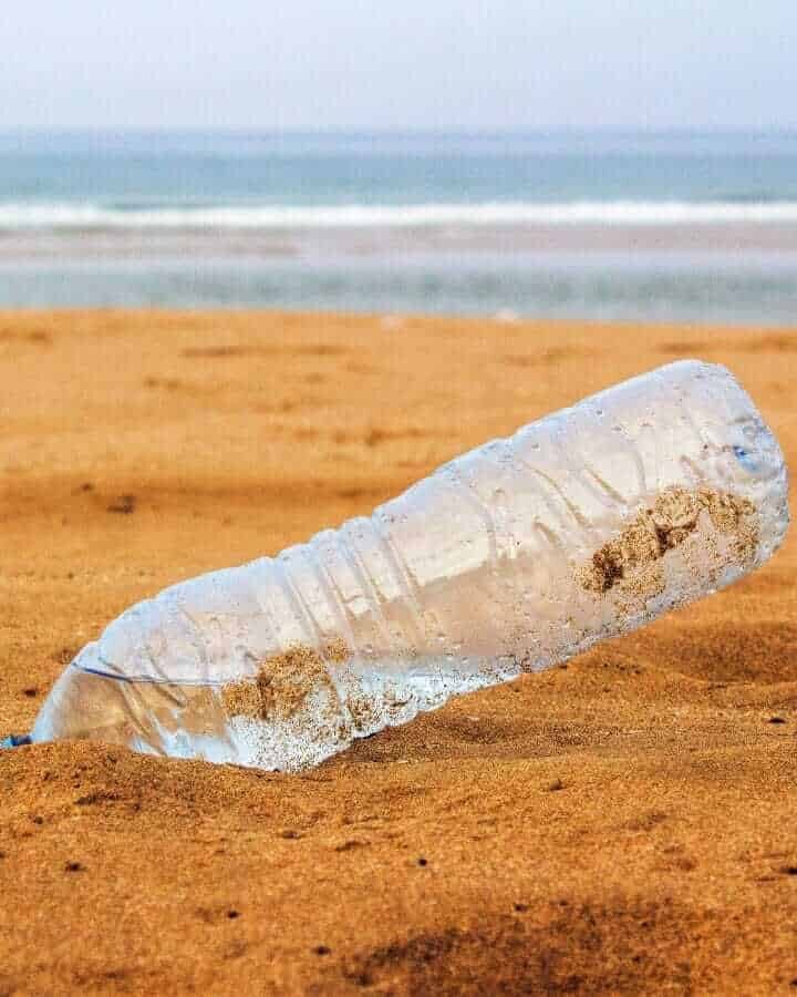 Plastik PET Flasche am Strand im Sand mit Meer im Hintergrund