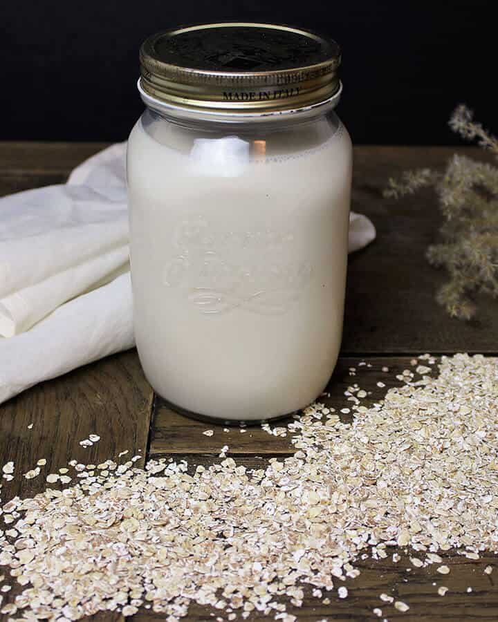 Hafermilch im Glas mit Haferflocken und Passiertuch