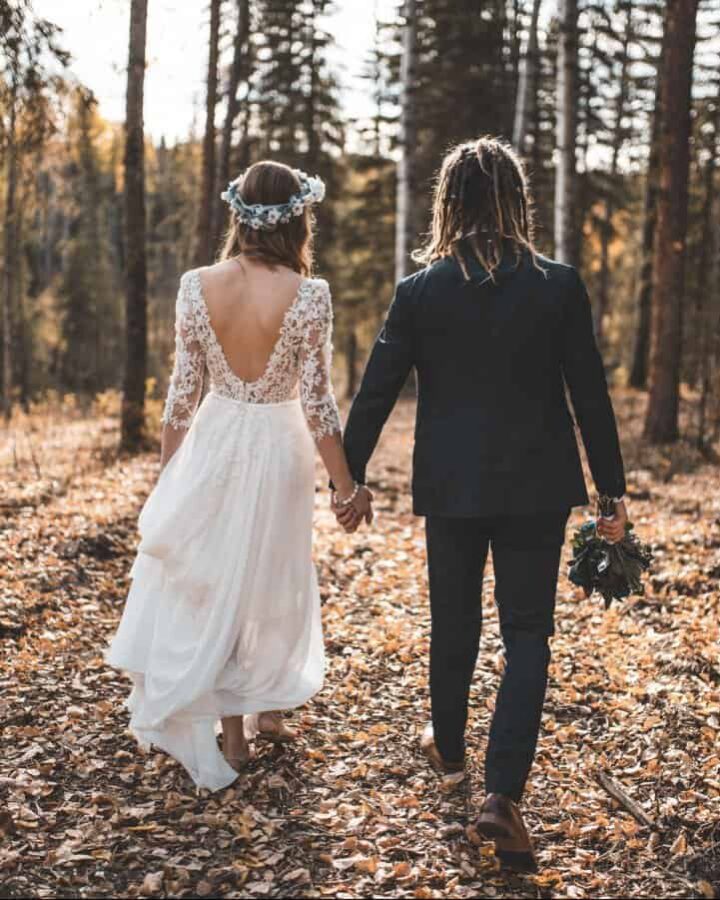 Boho Brautpaar von hinten Händchen haltend im Wald