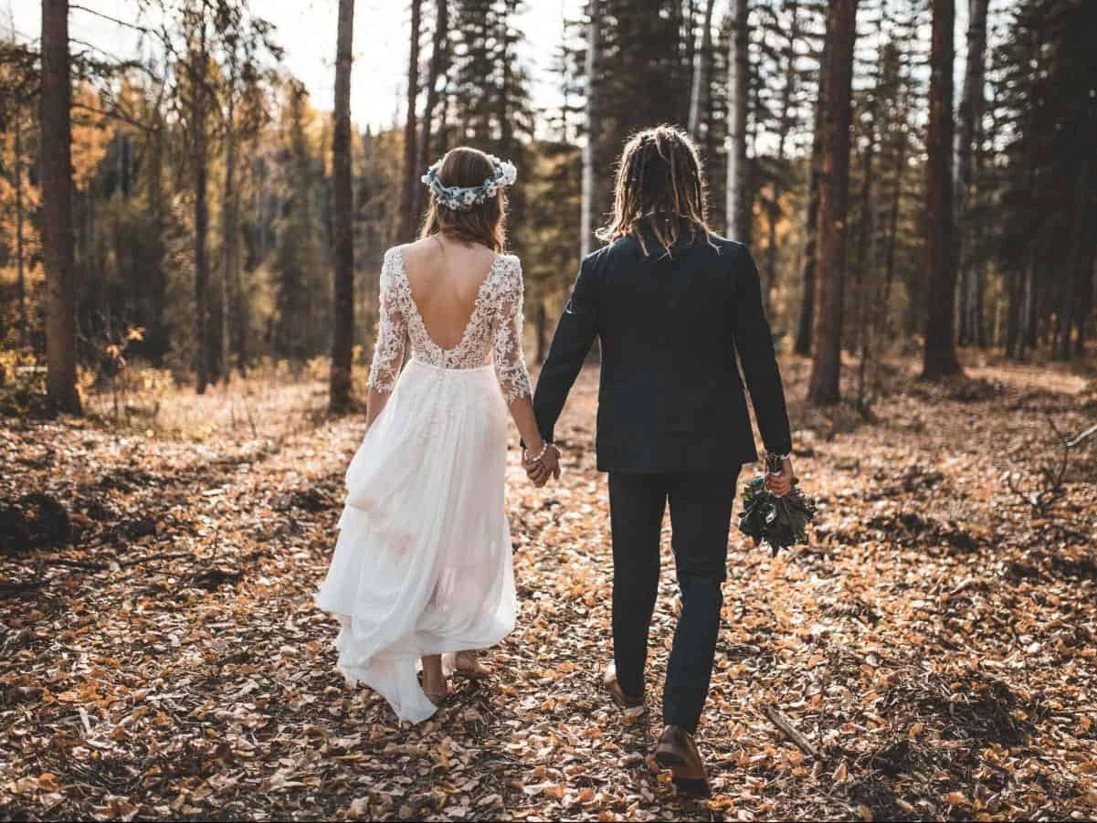 Boho Brautpaar von hinten Händchen haltend im Wald