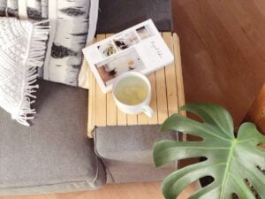 Sofatablett selbstgebaut mit Teetasse und Buch auf Sofa neben Monstera Pflanze und Makramee Kissen