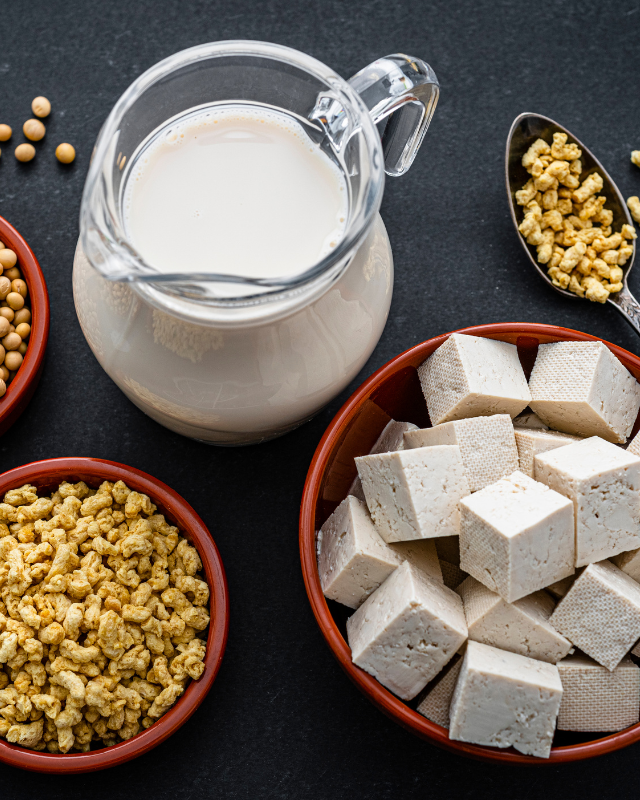 Sojabohnen, Tofu, Sojamilch und Sojaschnetzel auf einem schwarzen Tisch