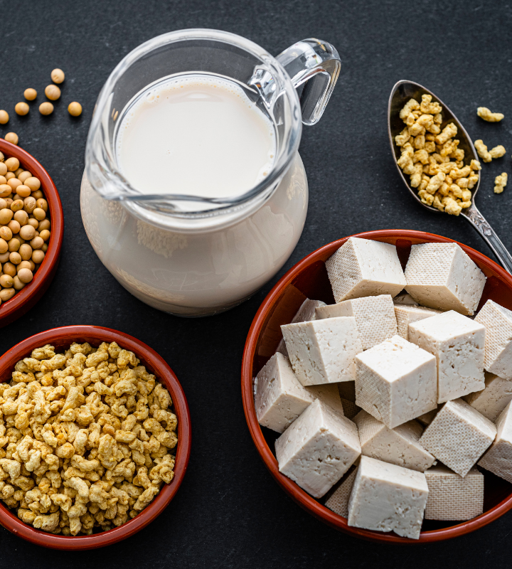 Sojabohnen, Tofu, Sojamilch und Sojaschnetzel auf einem schwarzen Tisch