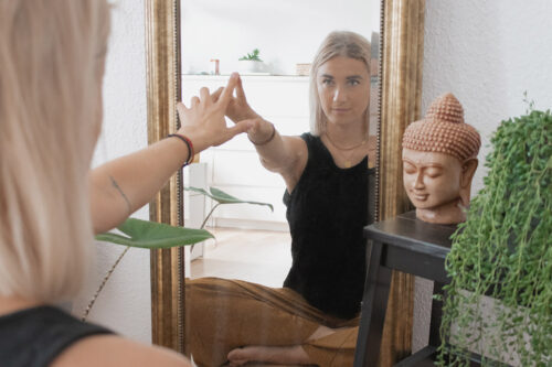 Frau schaut lächelnd in Spiegelbild und berührt mit Finger das Spiegelbild