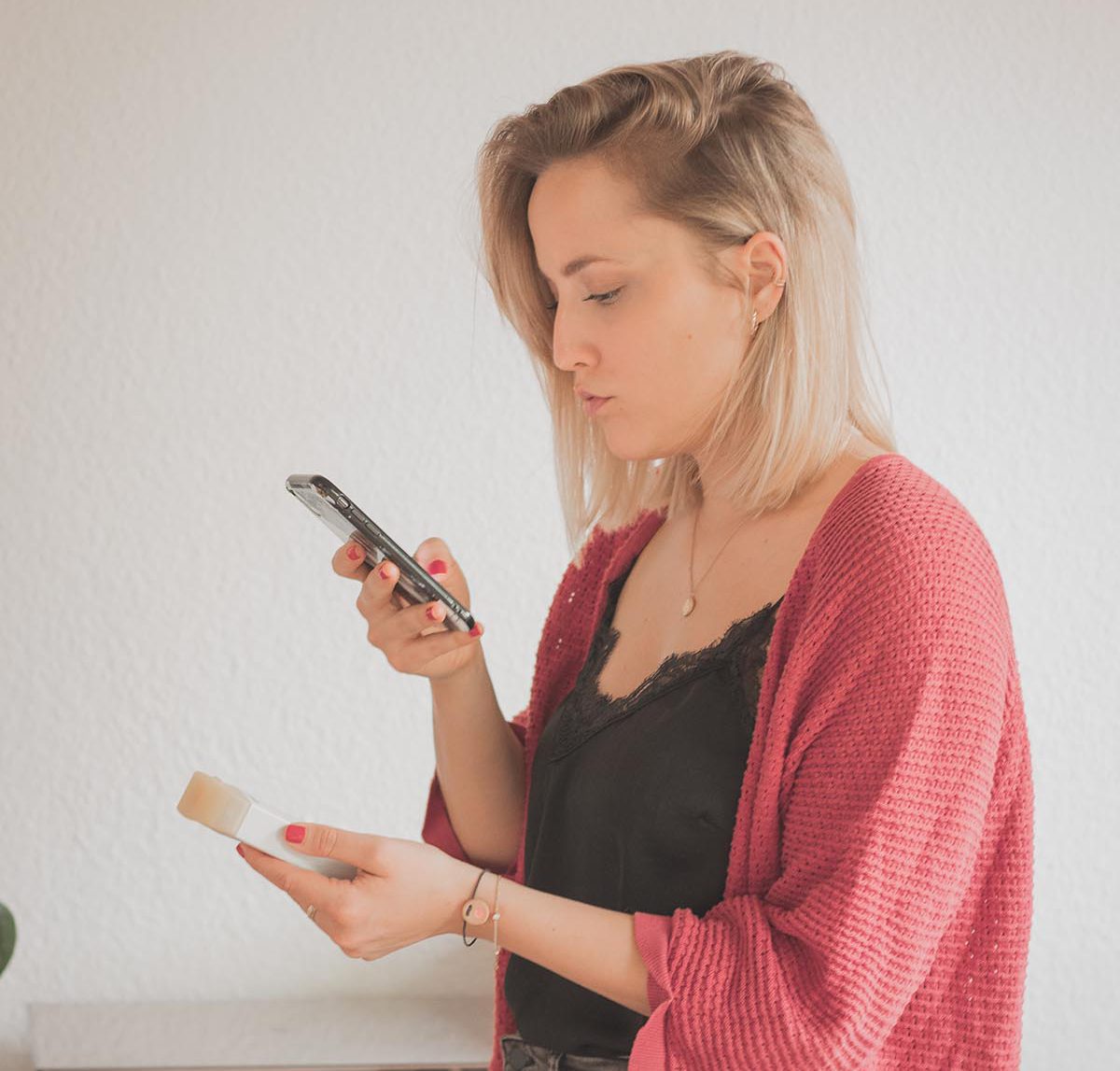 Frau prüft Inhaltsstoffe ihrer Kosmetik mit App auf dem Smartphone