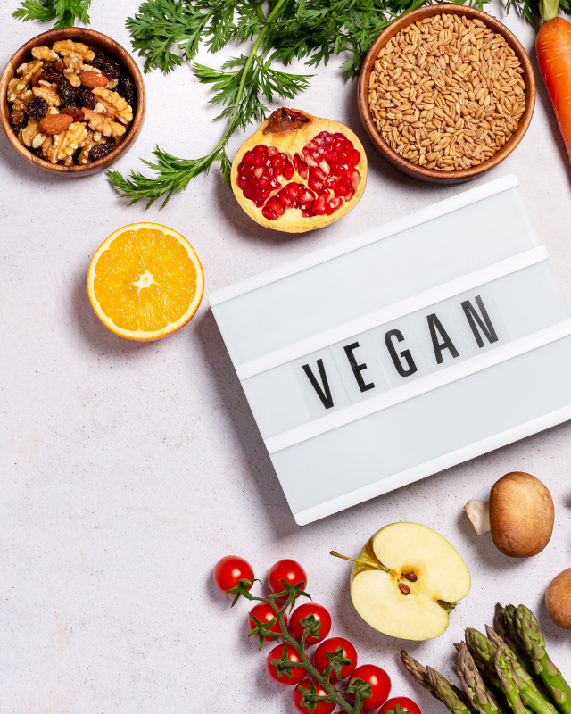Orangen, Karotten, Äpfel, Tomaten und anderes Gemüse und Obst liegen um eine Lichtbox mit der Aufschrift "vegan"