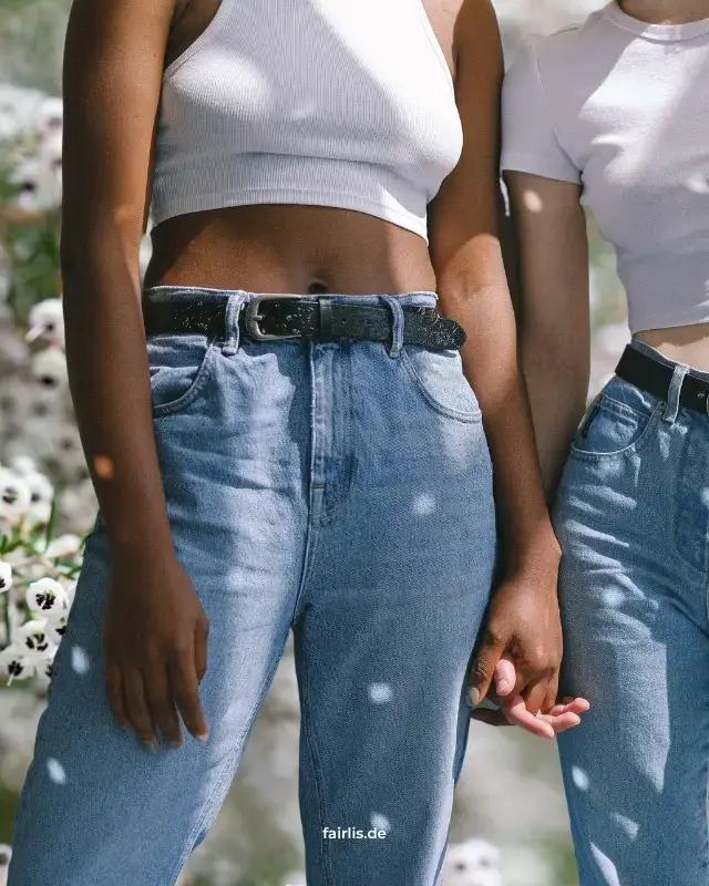 Zwei Frauen halten Hände, tragen Jeans und weiße Shirts, stehen vor weißen Blumen