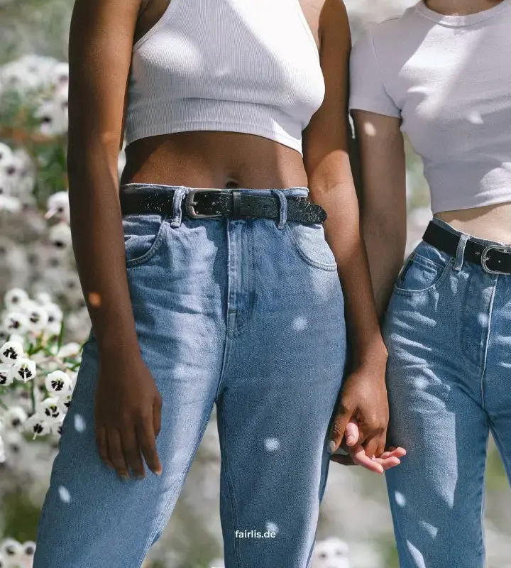 Zwei Frauen halten Hände, tragen Jeans und weiße Shirts, stehen vor weißen Blumen