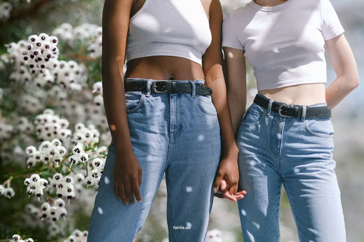 Zwei Frauen halten Hände, tragen Jeans und weiße Shirts, stehen vor weißen Blumen