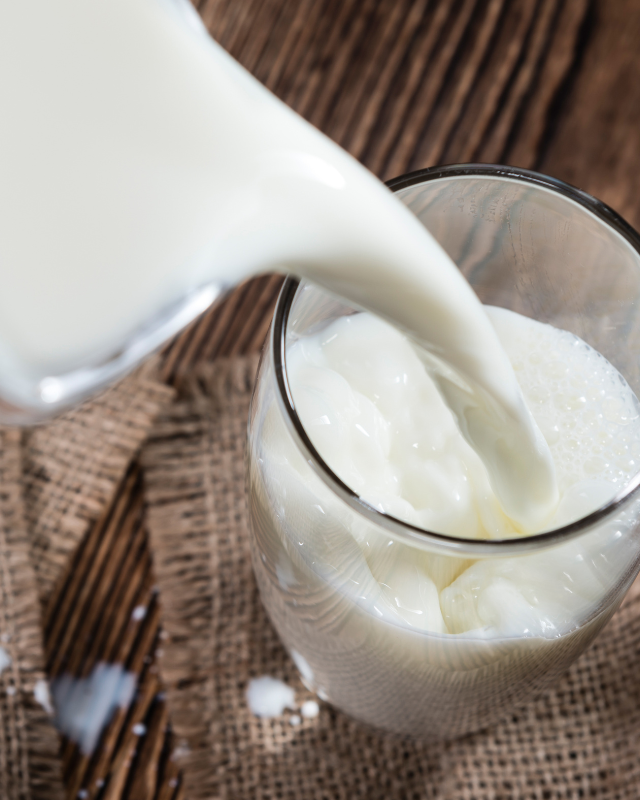 Milch aus Milchkanne wird in Glas eingeschänkt