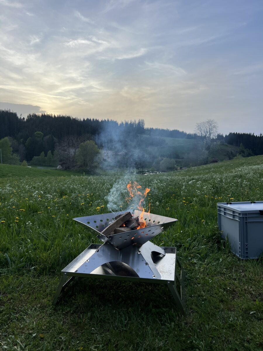 Feuerschale von Winnerwell, im Hintergrund eine Sommerwiese, Wald und Hügel