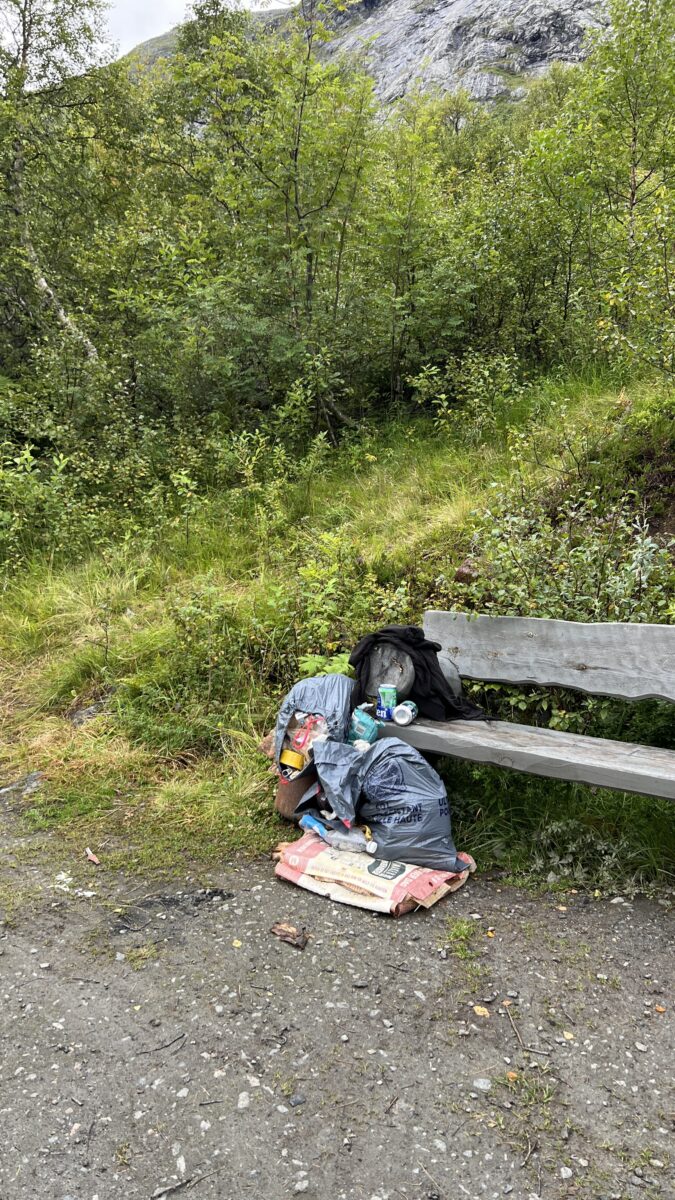 Eine große Tüte Müll und eine kaputte Luftmatratze auf einer Bank mitten in der norwegischen Natur.