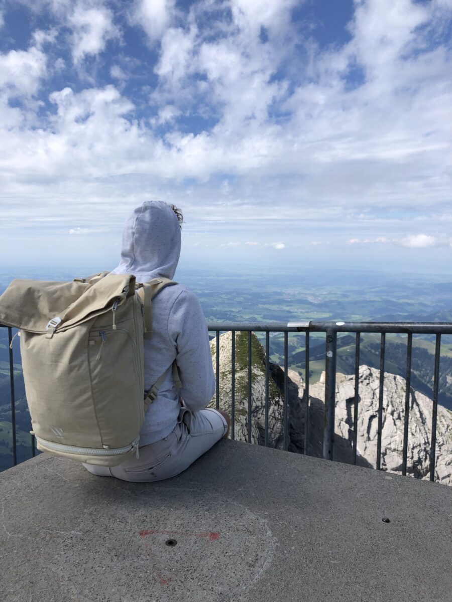 Ein Mann sitzt auf einem Aussichtsturm, der Blick geht in die Ferne, er trägt einen WAYKS Rucksack.